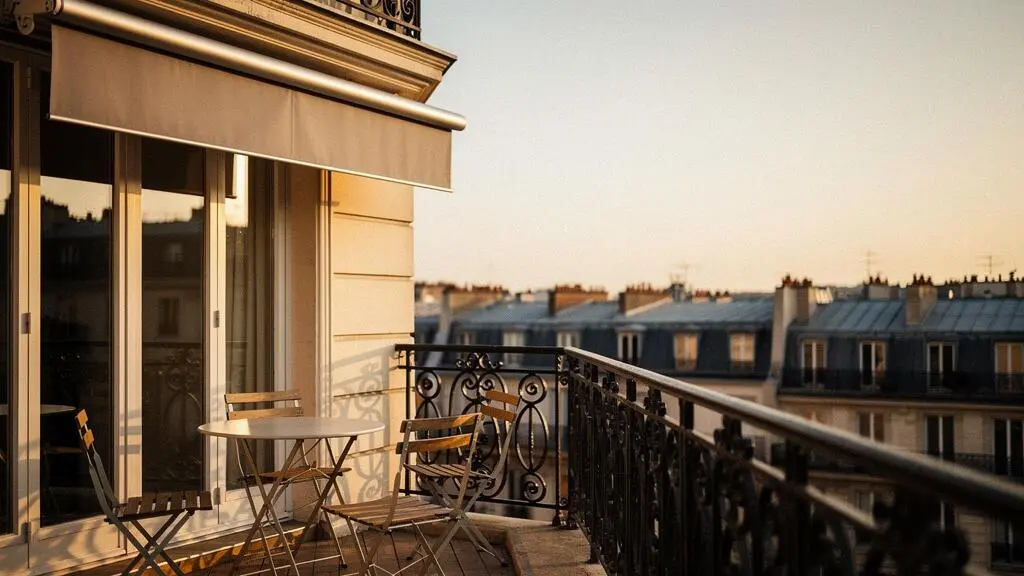 Balcon parisien baigné de lumière dorée avec un store banne entièrement enroulé, offrant une vue dégagée sur les toits