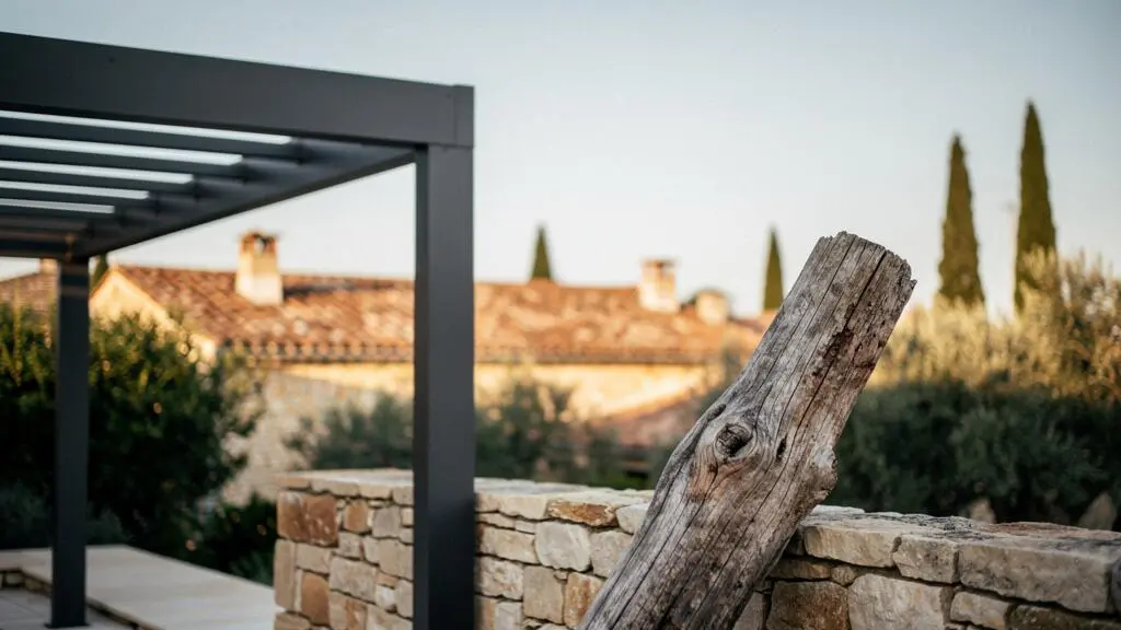Structure de pergola en aluminium impeccable contrastant avec une ancienne poutre en bois vieillie, sur une terrasse française baignée de lumière naturelle