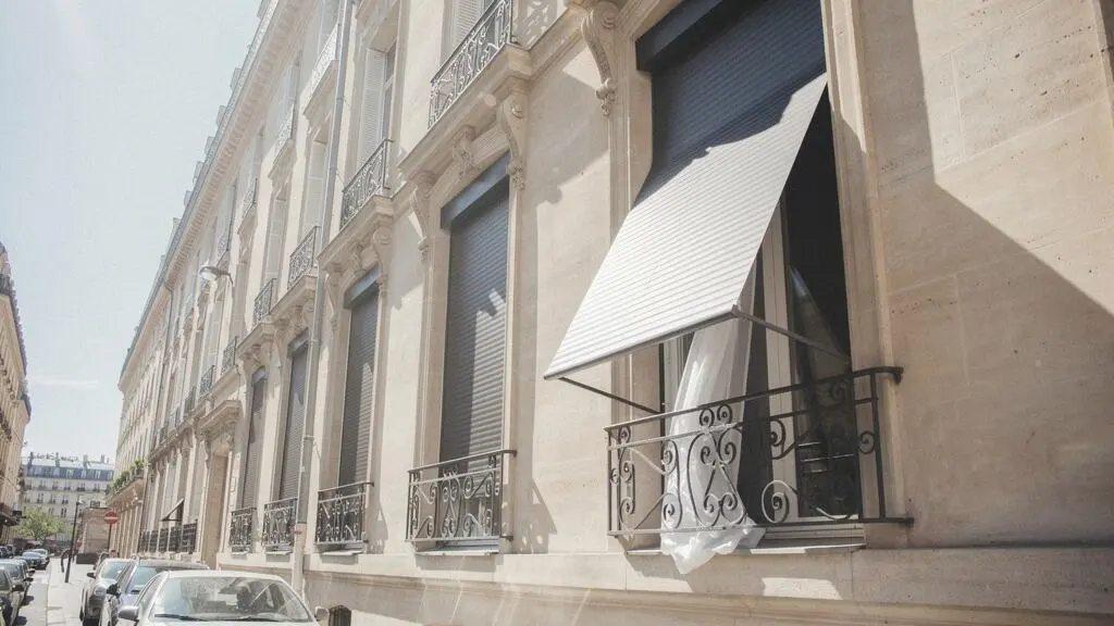 Façade d'un appartement parisien avec des stores extérieurs baissés protégeant l'intérieur de la chaleur estivale