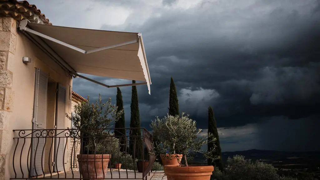 Terrasse d'une maison française avec store banne se refermant automatiquement alors qu'un ciel d'orage menaçant approche