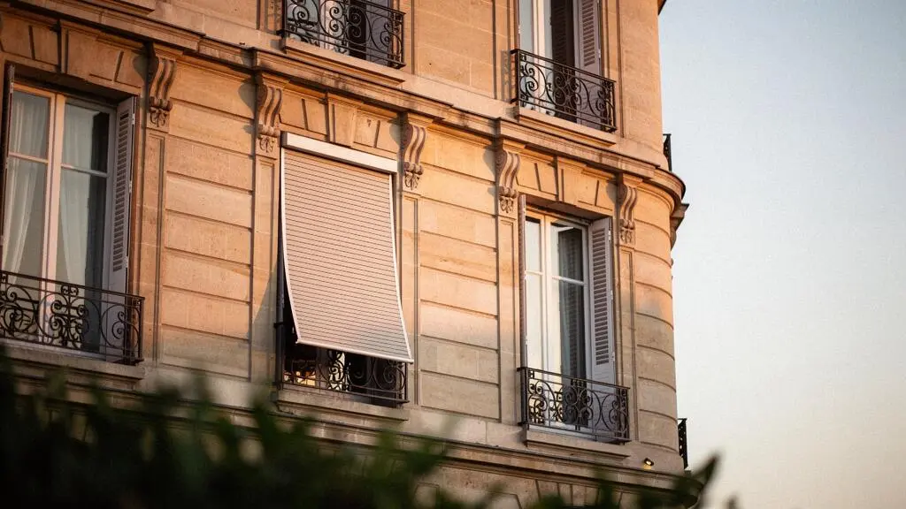 Store extérieur motorisé à demi-fermé sur la façade d'une maison française traditionnelle en fin de journée, symbolisant sécurité et économie d'énergie